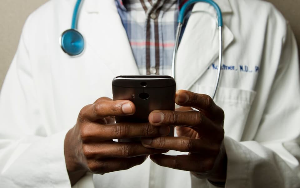 Arzt der Clinovita-Praxisgruppe im weißen Kittel mit Stethoskop und Smartphone